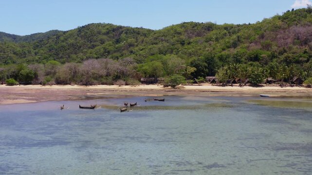 4K drone video flying over shallow coastal waters towards traditional wooden canoes anchored near the beach at Lokobe Nature Reserve in Nosy Be, Madagascar.