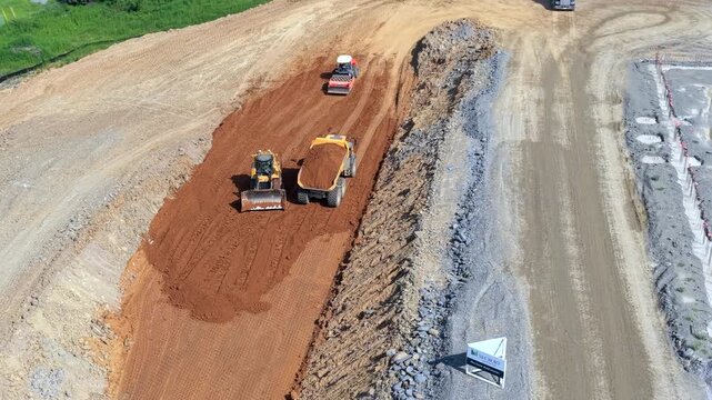 Heavy machinery - crawler bulldozer, dump truck, and tracked loader preparing and leveling a construction foundation - aerial parallax
