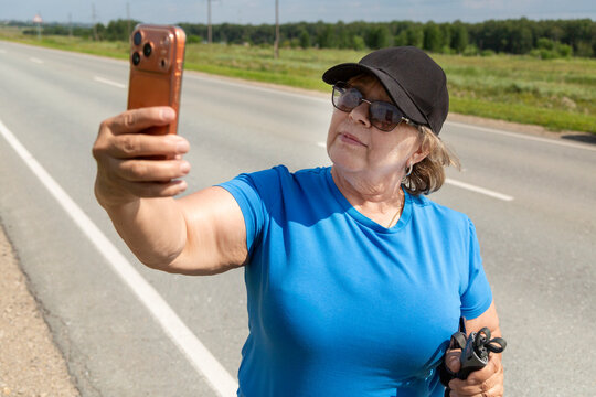 Woman taking selfie outdoors on highway holding phone and camera