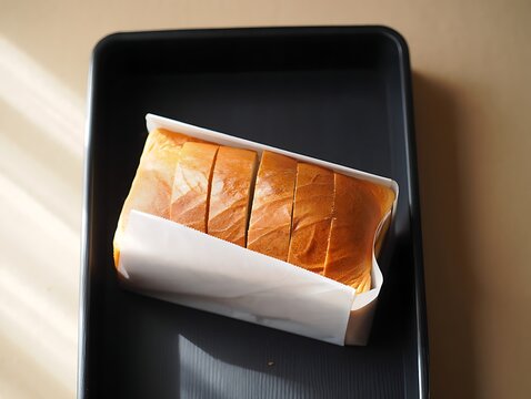 Freshly baked slices of white bread served in a black tray under soft natural morning sunlight