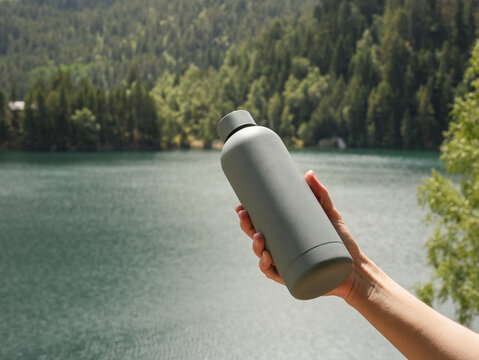 Hand Holding Reusable Water Bottle Against Mountain Lake