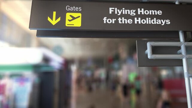 Airport terminal sign with the message Flying Home for the Holidays in focus, with a bustling, out of focus background of travelers walking through the concourse during a busy travel season
