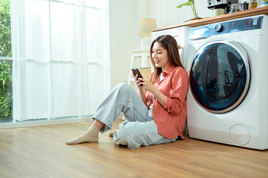 Woman Sitting by Washing Machine at Home Using Smartphone and Enjoying Her Time