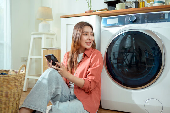 Woman Sitting by Washing Machine at Home Using Smartphone and Enjoying Her Time