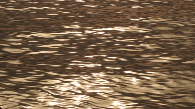 Close up of wavelets and ripples on the sea surface glistening with bright golden sunlight during sunset