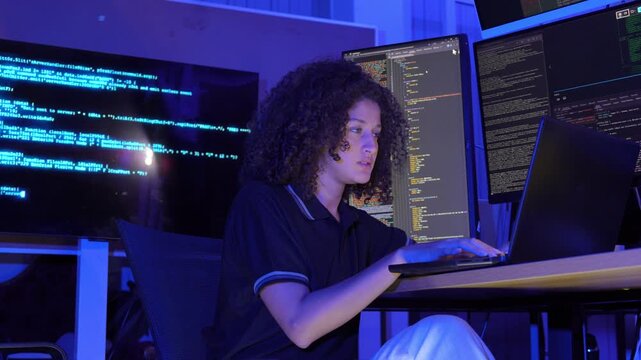 Female software developer working with multiple monitors display programming code in a modern technology workspace. coding, cybersecurity, digital technology, data processing, programming, innovation.