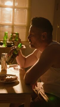 Vertical video of depressed middle aged Caucasian man drinking beer from bottle indoors. Clip fits substance abuse campaigns and mental health recovery projects