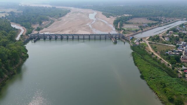 Wide aerial perspective of a concrete water diversion barrage and irrigation canal alongside a vast dry riverbed in Nepal