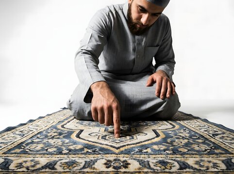 Muslim man in traditional clothing kneeling on prayer rug against white background