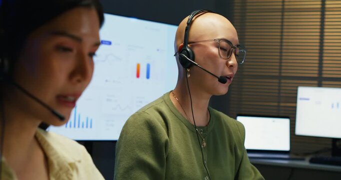 Asian women operators managing customer interactions. Two colleagues talking and working at a desk with multiple screens, providing reliable digital communication and service.