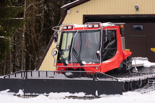 A snowplow on red tracks standing in winter in the forest near the barn