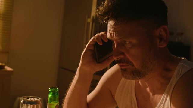 Caucasian middle aged man talking on mobile phone and drinking beer from bottle. Clip fits commercial advertising for addiction recovery programs, mental health support, and substance abuse PSAs