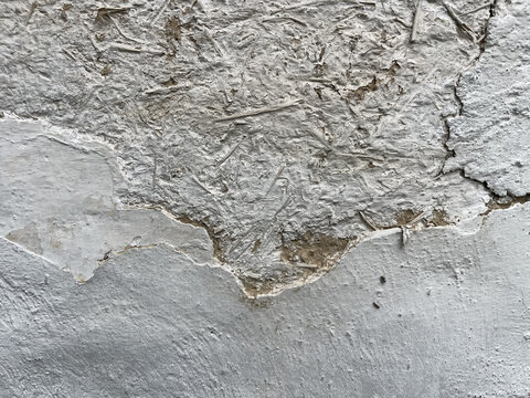Full frame background texture of weathered white stucco peeling off an old adobe clay wall with straw