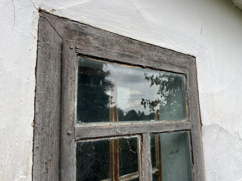 Horizontal low angle shot of an old weathered wooden window frame on a white stucco wall with glass reflection