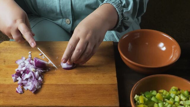 Hands chop red onions with a knife on a cutting board on the table