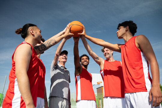 Diverse male basketball players in red jerseys celebrating team unity together on court