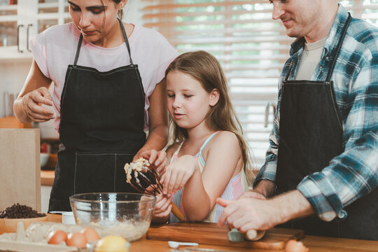 Family cooking concept with parents and daughter preparing homemade food together in a bright kitchen, sharing baking skills and quality time. family, cooking, kitchen, baking, together