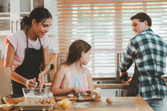 Family cooking concept with parents and daughter preparing homemade food together in a bright kitchen, sharing baking skills and quality time. family, cooking, kitchen, baking, together