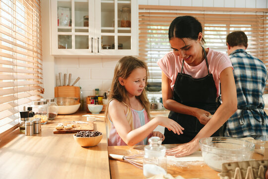 Family cooking concept with parents and daughter preparing homemade food together in a bright kitchen, sharing baking skills and quality time. family, cooking, kitchen, baking, together
