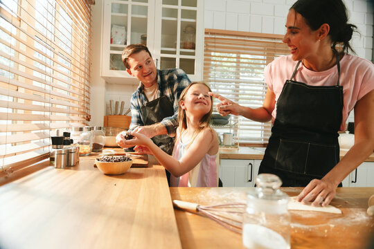 Family cooking concept with parents and daughter preparing homemade food together in a bright kitchen, sharing baking skills and quality time. family, cooking, kitchen, baking, together