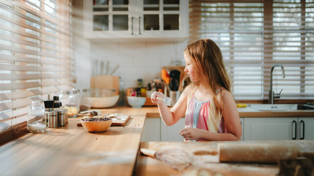 Child baking concept with young girl preparing homemade food alone in a bright kitchen, using a pastry brush near baking ingredients. child, baking, kitchen, cooking, homemade