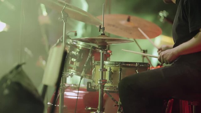 A man is playing drums on concert in front of a red drum set in slow motion. The drum set is surrounded by other instruments.