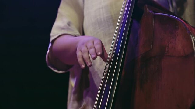 A woman playing a contrabass in slow motion and dark atmosphere. Concept of calm and focus as the woman plays the instrument