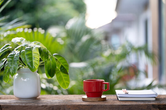 Red coffee cup and diary notebook with philodendron plant on wooden table