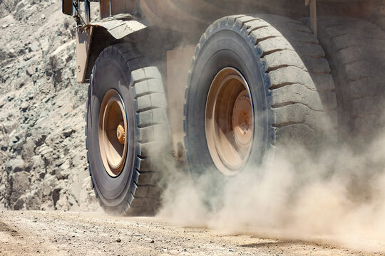 Close-up view of the thick cloud of dust and air pollution raised by the giant wheels of large mining trucks traveling along a dirt road in an open-pit mine.