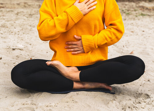 Close-up of woman practicing breathing exercise with hands on chest and belly on autumn beach
