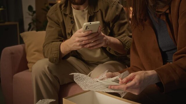 Young Caucasian couple examining broken plate from delivery box while man takes photos using smartphone. Perfect for e-commerce return and customer support ads