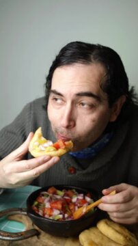 Close up view of a man eating golden sopaipillas topped with fresh pebre salsa, Man enjoying traditional Chilean fried sopaipilla bread with spicy tomato pebre