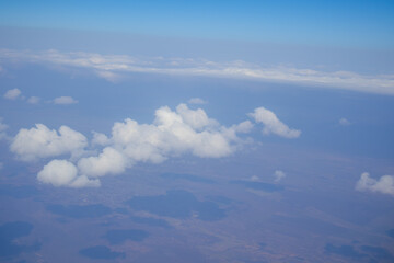Obraz premium White clouds casting shadows over countryside viewed from an airplane