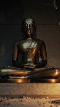Vertical video: Burner releasing smoke while bronze Buddha glowing in shrine alcove for meditation