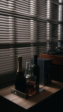 Vertical video of assorted alcohol bottles standing on tray near window blinds. Footage suitable for alcoholism awareness, addiction recovery campaigns, and mental health commercial projects
