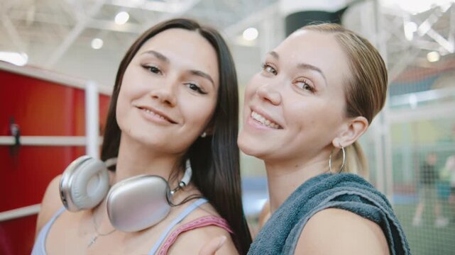POV Two sporty young women take a selfie while wearing athletic clothes inside a gym during a workout session