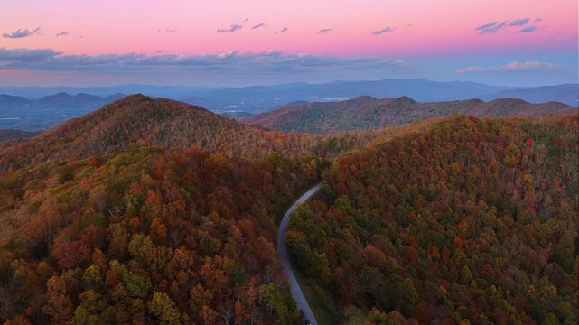 Car cruising on scenic road in Appalachian mountains at sunset. Trees glowing in vibrant fall foliage.