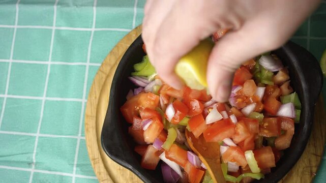 Squeezing fresh lemon juice over homemade pebre salsa in a ceramic bowl