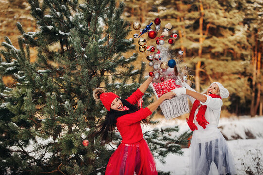 two girls near the Christmas tree throw a lot of toys on the tree. Christmas tree decoration on the street in winter.Lots of Christmas balls on the tree