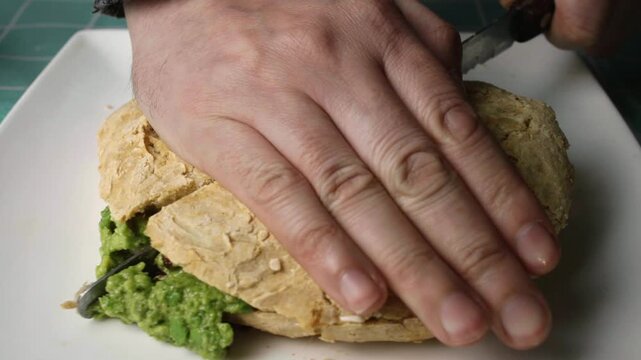 Close up view of hands cutting a gourmet pork and avocado sandwich in half