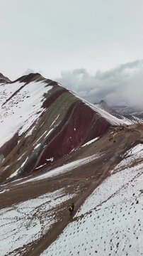 Aerial drone view of Rainbow Mountain Vinicunca in the Peruvian Andes, with multicolored peaks partly covered in snow. Tourists hiking up the mountain. Located in the Cusco region, Peru. 