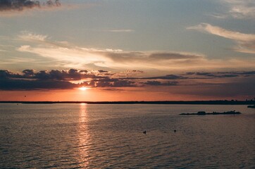 Fototapeta premium Scenic sunset with an orange sky over a wide river or lake featuring small silhouettes of boats. Analog 35mm film photography.