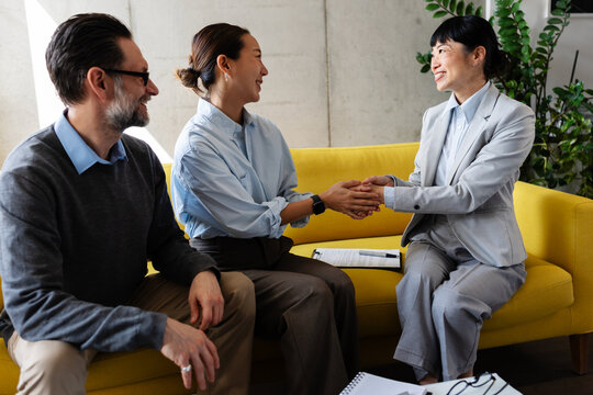 Happy home buyer shaking hands with a real estate agent after a successful property consultation while her partner smiles beside them