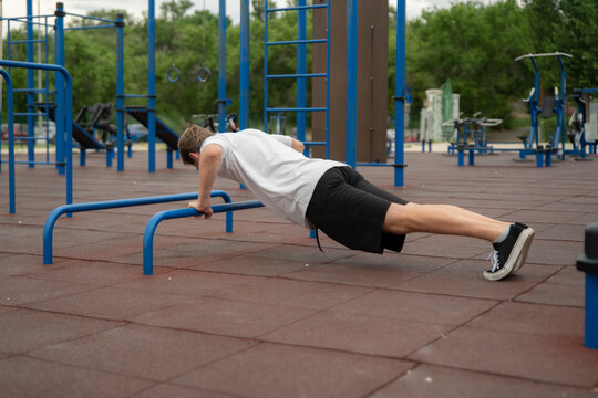 A man is exercising at an outdoor gym using parallel bars for push-ups during the day