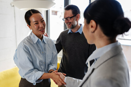 Happy female home buyer shaking hands with a real estate agent after viewing a property while her partner smiles beside her.