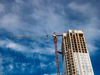 Construction site with a high-rise building under construction and a tower crane against a cloudy blue sky © LemPro Filming Life