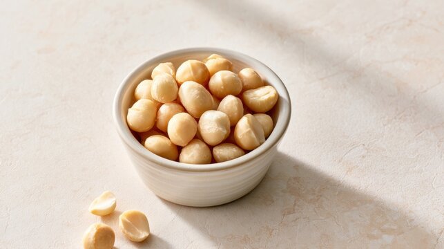 Bowl of macadamia nuts on light stone surface, healthy snack ingredient, baking and nutrition concept