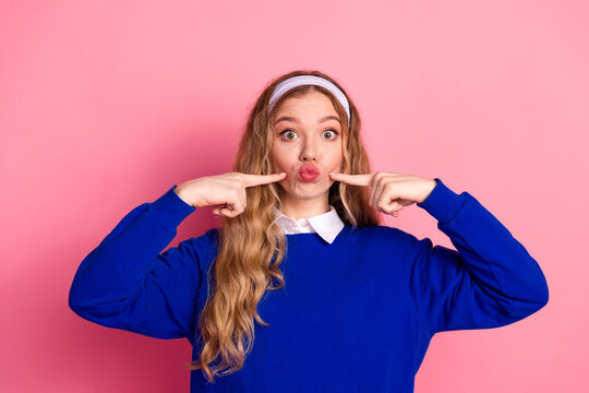 Playful young girl in blue sweater poses with pink background making kissy pout for fashion lifestyle stock photo