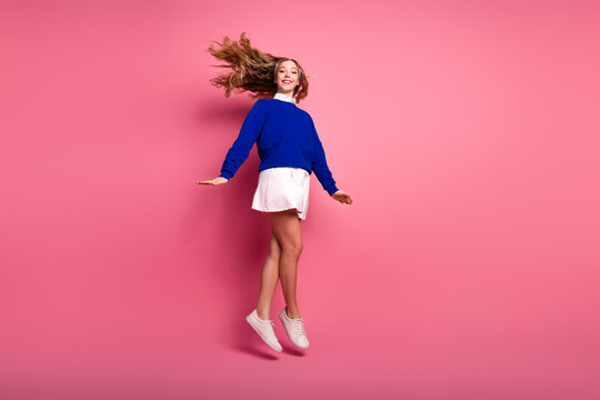 Happy young girl jumps in blue sweater white skirt on pink background studio shot