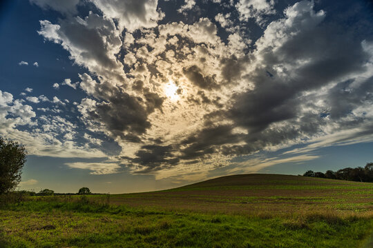 Dramatic Sunburst Through Fluffy Clouds Over Rolling Green Hill